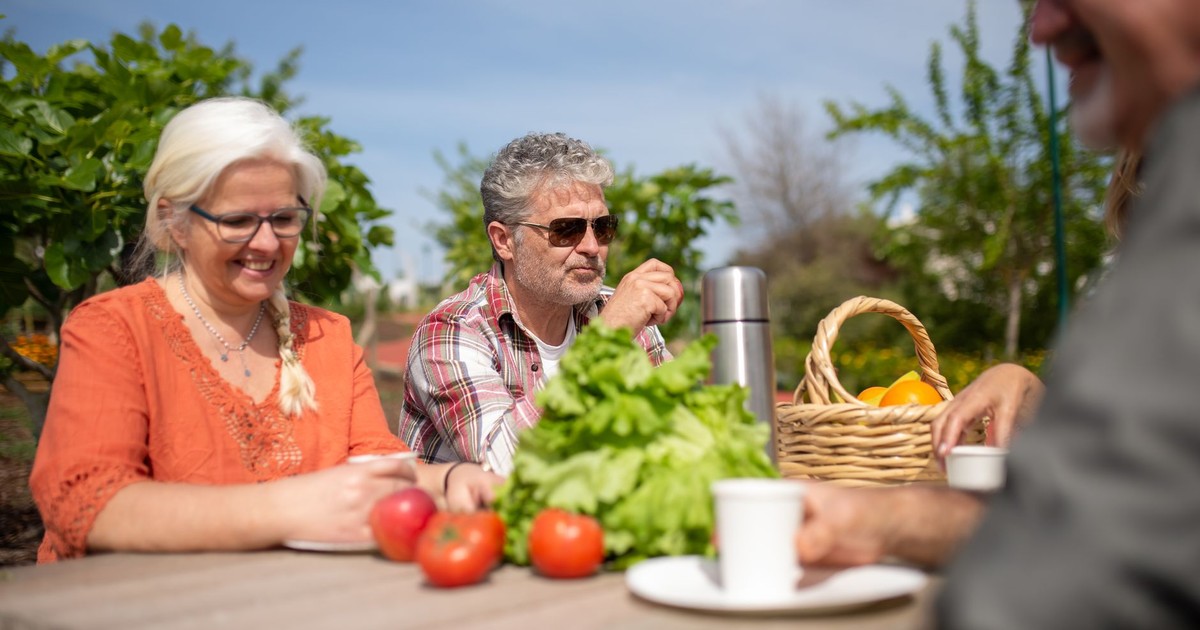A group of senior friends enjoying a casual outdoor lunch together with fresh vegetables.
