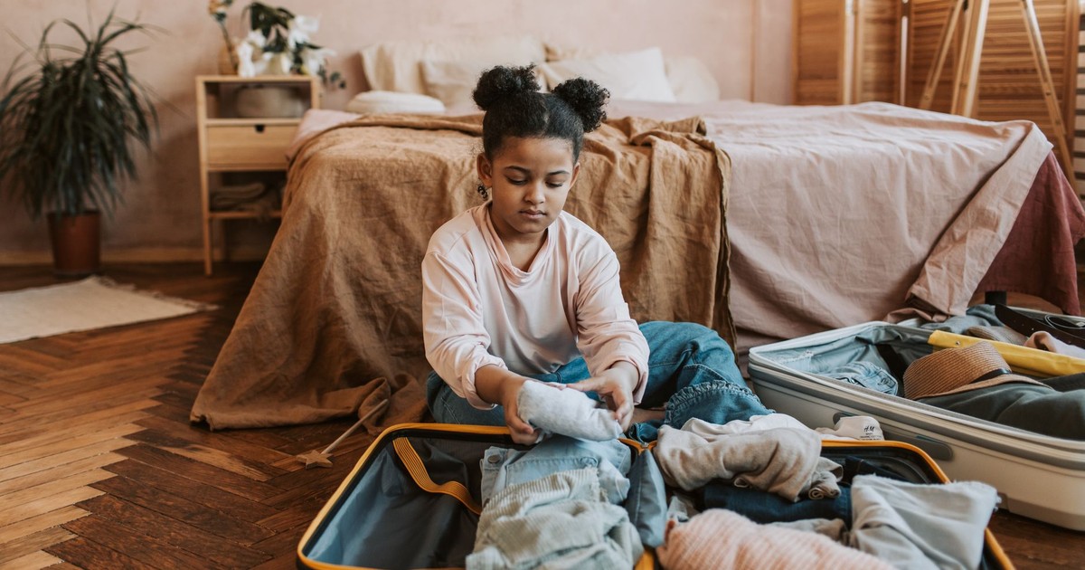 A young girl folding clothes into a suitcase in a cozy bedroom setting with natural decor.