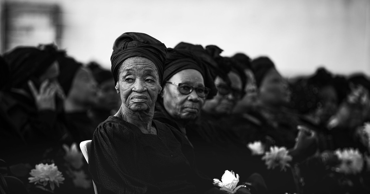 Elderly women in Kinshasa mourn together at a solemn funeral in monochrome.