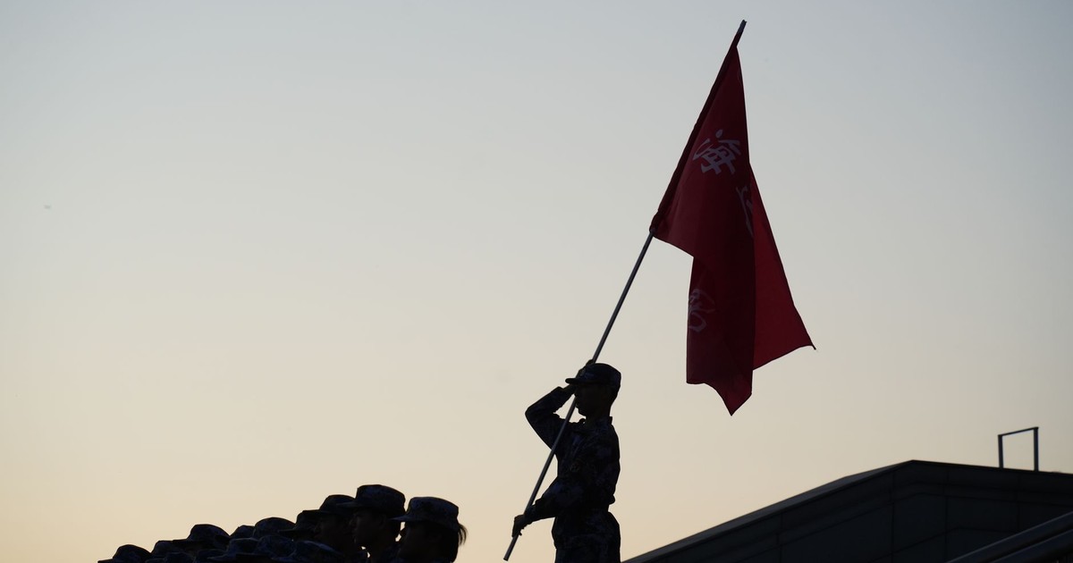 A soldier salutes with a flag during a parade at sunset, creating a striking silhouette.