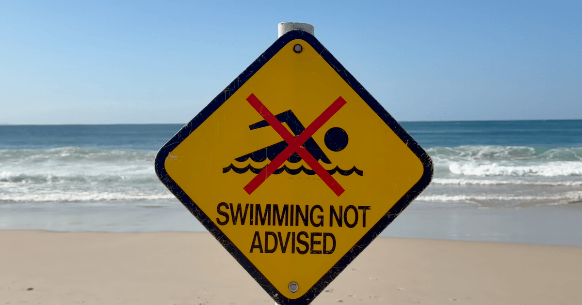 Warning sign on Byron Bay beach advising against swimming due to safety concerns.