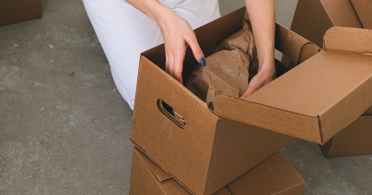 From above of crop anonymous relocating female packing wrapped items into carton box while preparing for moving to new apartment