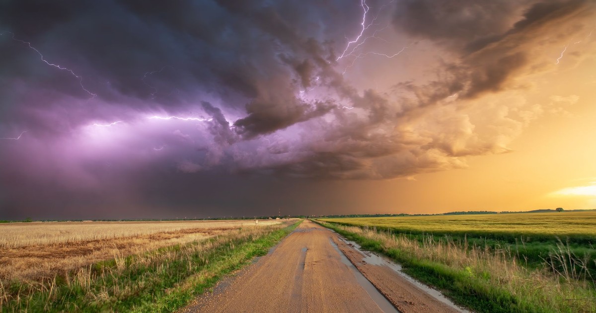 Stunning photo of a thunderstorm with lightning over a wheat field and dirt road in Oklahoma.