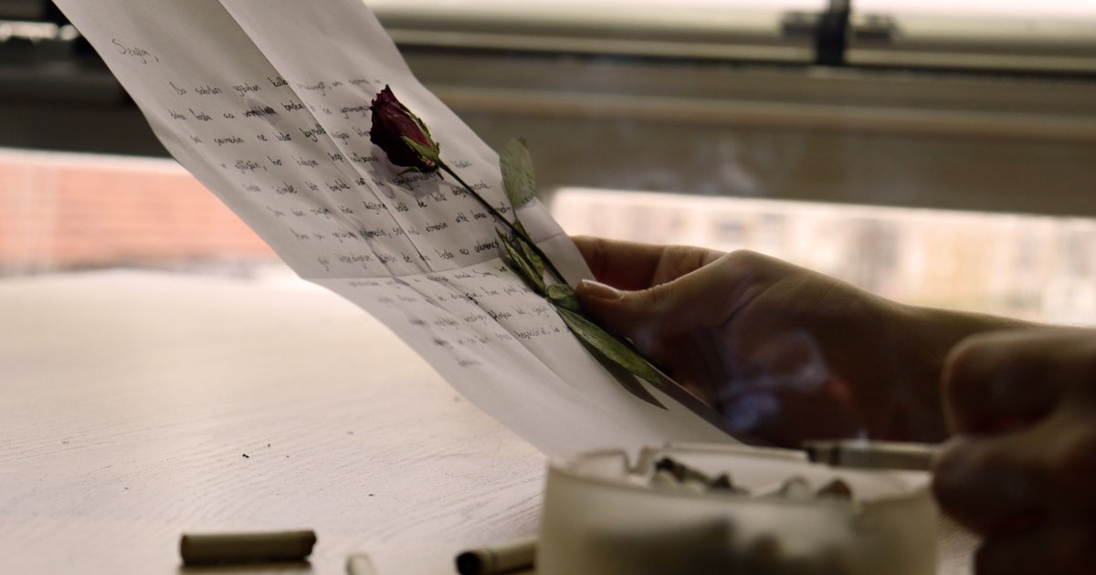A person holding a letter with a red rose and ashtray; evokes nostalgia and introspection.