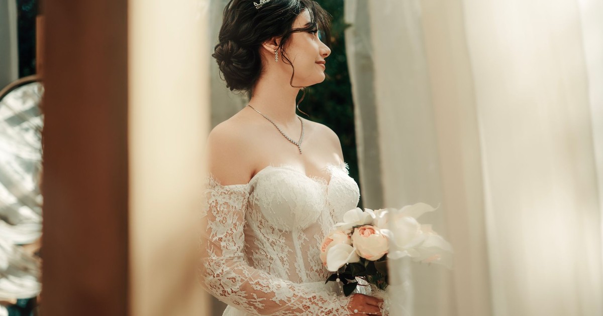 A beautiful bride in lace dress holding a bouquet, standing during her wedding ceremony.