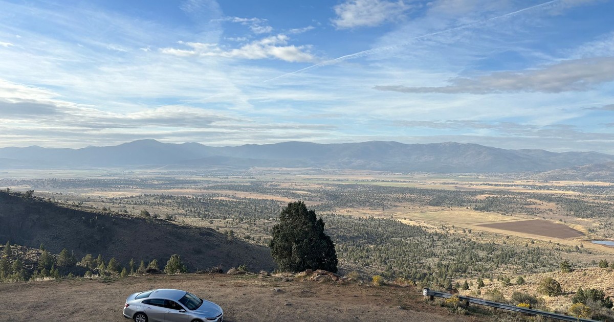 A silver car parked on a desert overlook in Nevada, offering a stunning valley and mountain view.