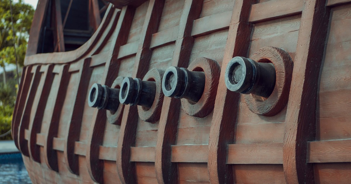 Side view of a historic wooden ship, showcasing canons and detailed wooden planks.