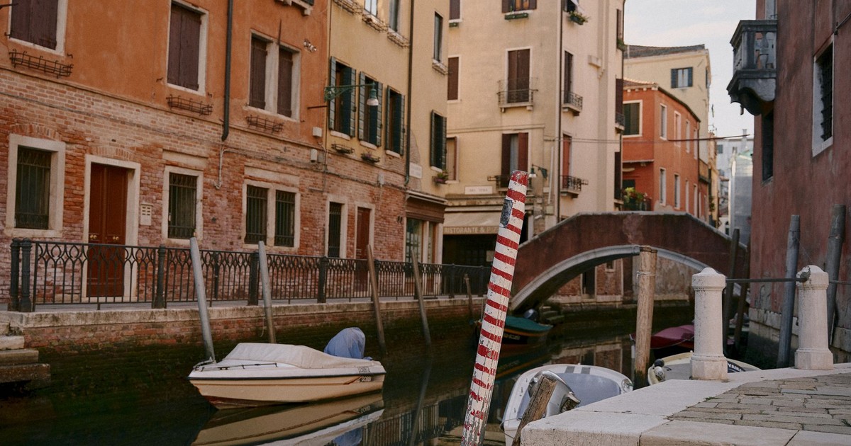 Explore a tranquil Venetian canal scene featuring colorful buildings, a bridge, and boats.