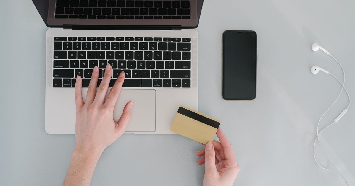 Flat lay of a workspace with a laptop, bank card, smartphone, and earphones, ideal for online finance themes.