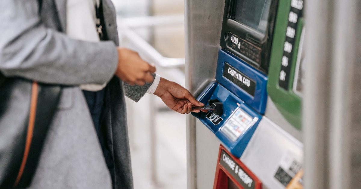 Side view of crop unrecognizable female in stylish clothes using credit card while buying metro ticket via electronic machine
