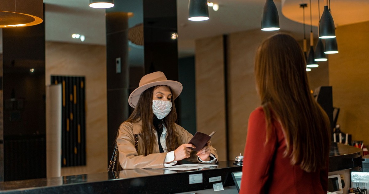 A woman wearing a mask checks in at a hotel reception desk.