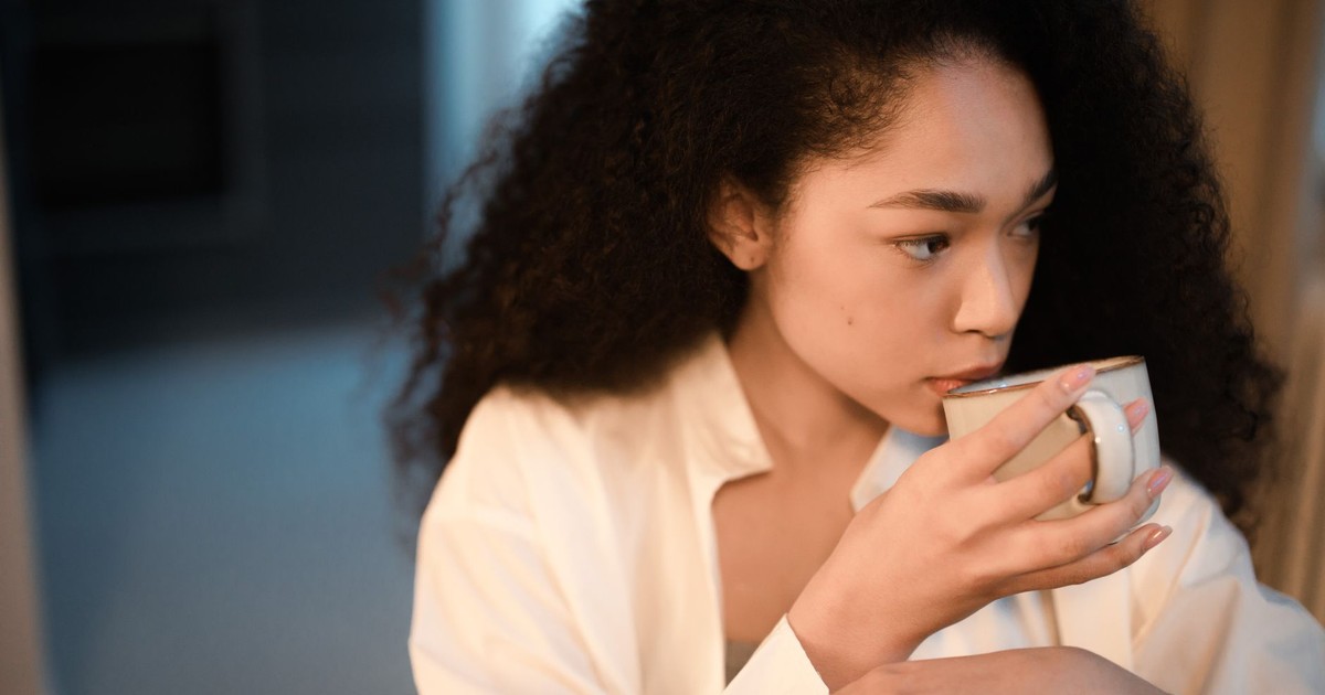 A woman with curly hair savoring a cup of coffee indoors, embracing a peaceful morning atmosphere.