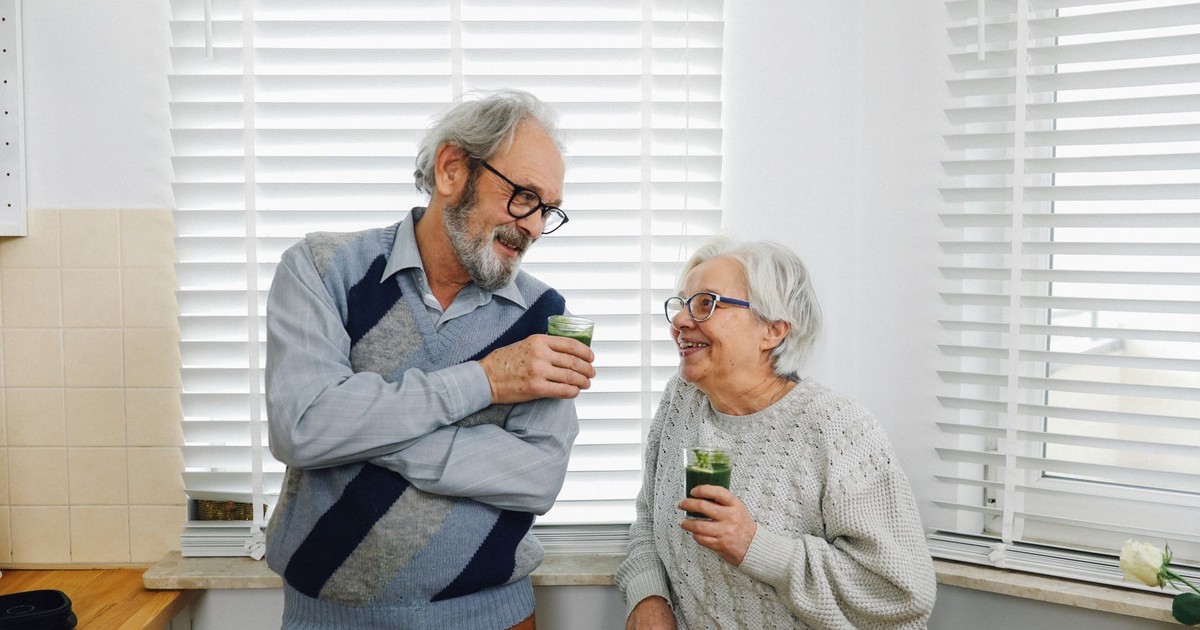 Senior couple smiling and enjoying green smoothies in a cozy kitchen setting.