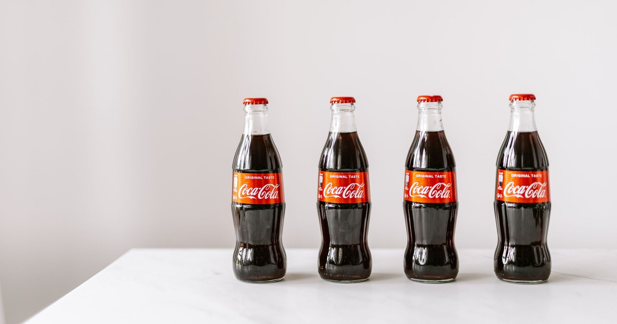 Glass bottles full of fresh soft drink placed on white table in row