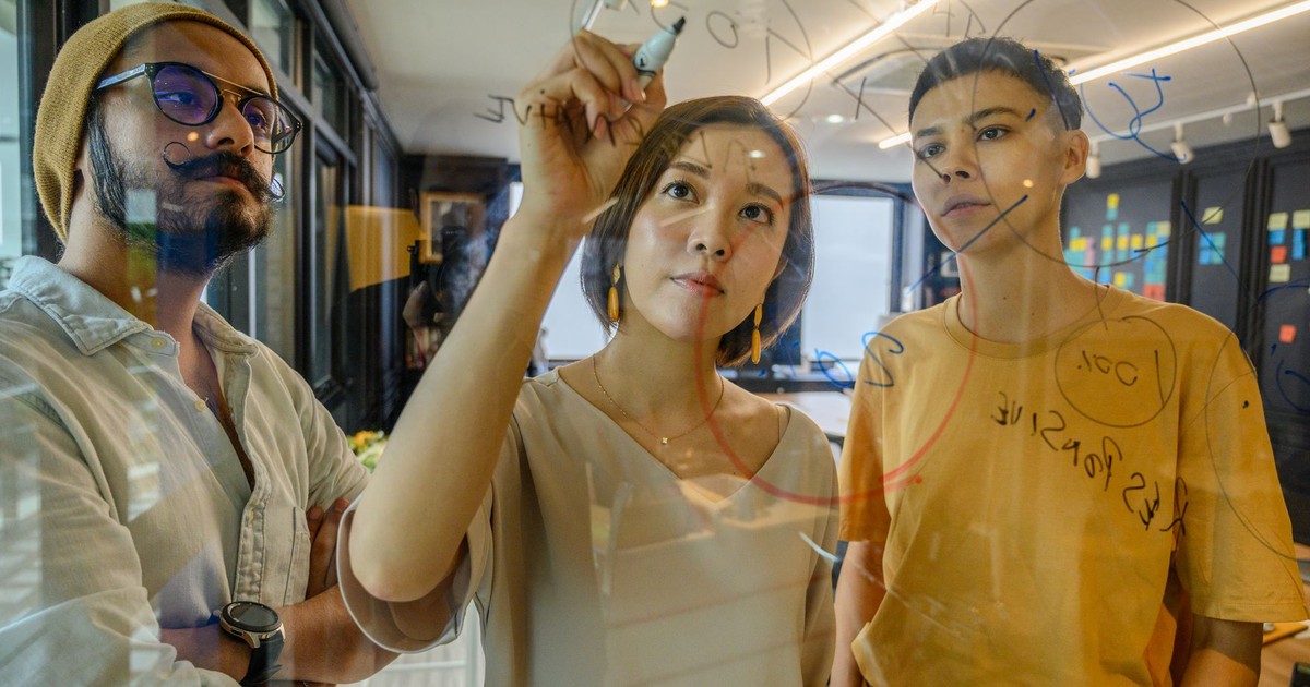 Three colleagues engaged in a strategy meeting, writing ideas on glass in a modern office.