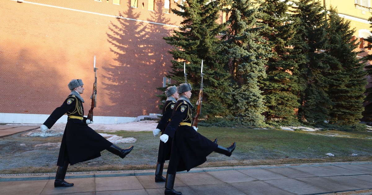 Ceremonial guards march outside the Kremlin walls in Moscow on a bright day.
