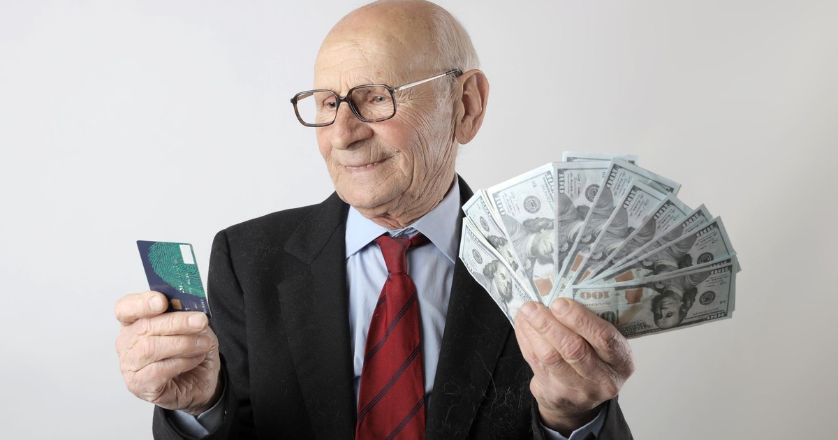 Elderly man in a suit holding a credit card and US dollar bills, representing finance and wealth.