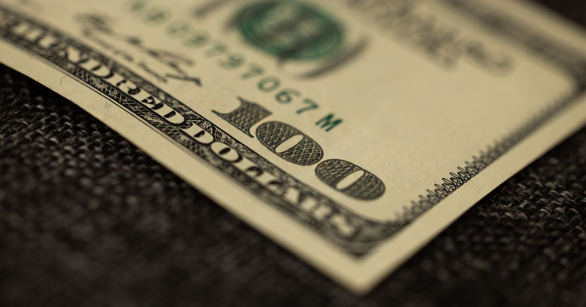 Detailed close-up of a hundred dollar bill resting on dark fabric surface, showcasing texture.
