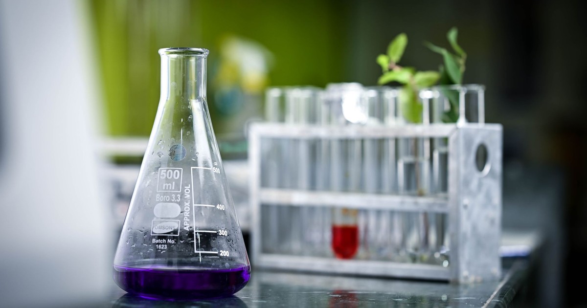 Close-up of a lab flask with purple liquid and test tubes in a scientific setting.