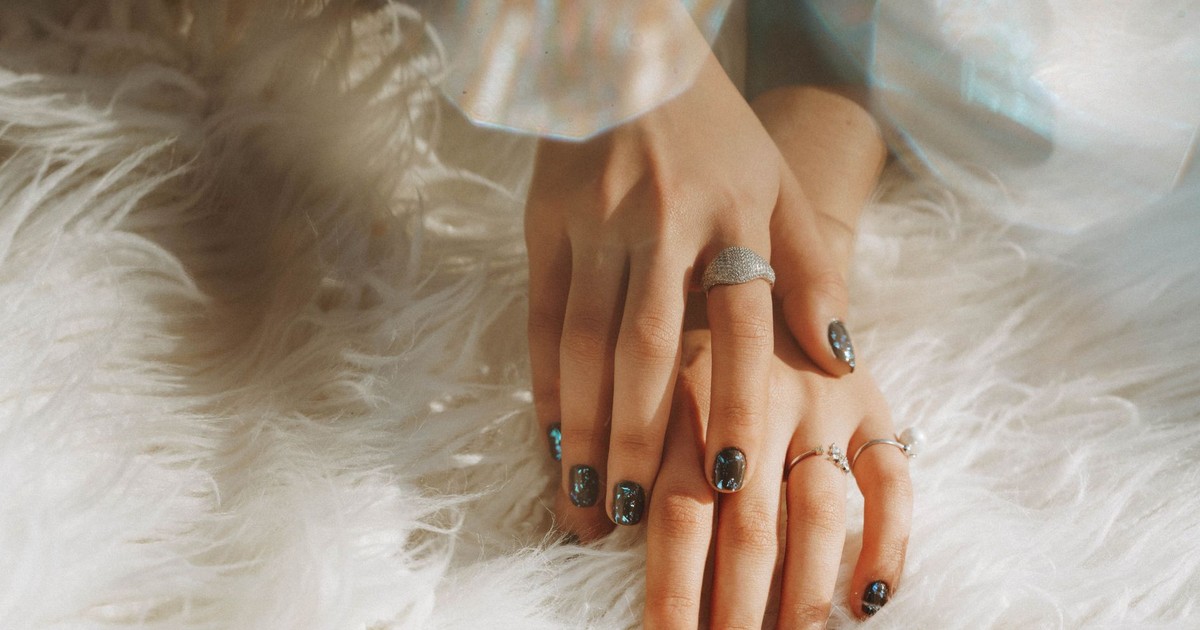 Close-up of a woman's hands wearing rings and nail art, resting on white faux fur.