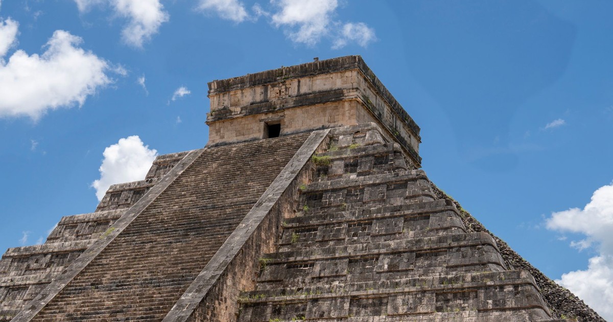 Explore the iconic stepped pyramid of Chichén Itzá against a bright blue sky.