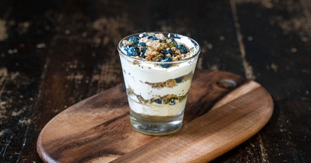 Delicious blueberry yogurt parfait layered with granola, served in a glass on a wooden board.