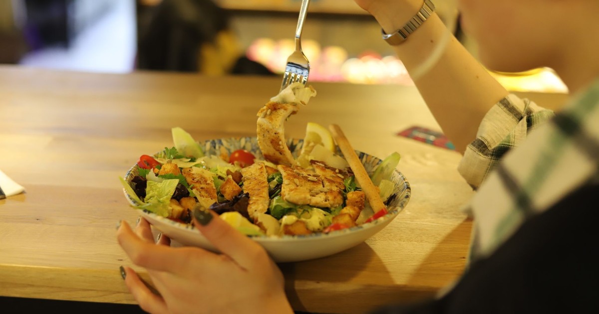 Close-up of a person enjoying a fresh chicken salad at a wooden table indoors.