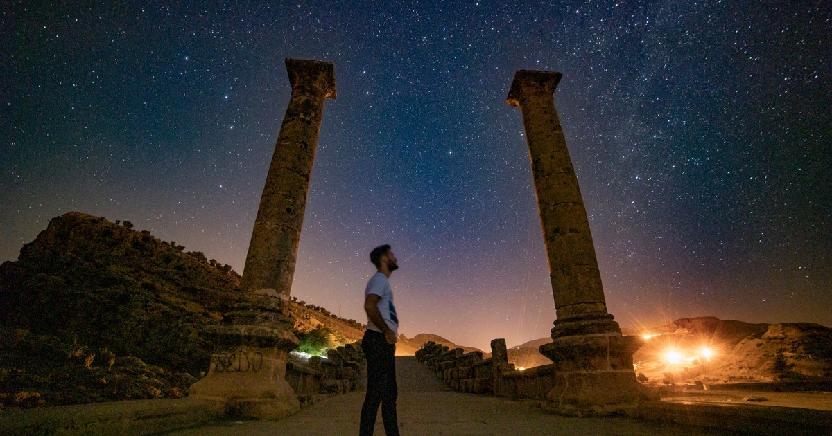 Man stands among ancient columns under a starry night sky, capturing serene beauty and history.