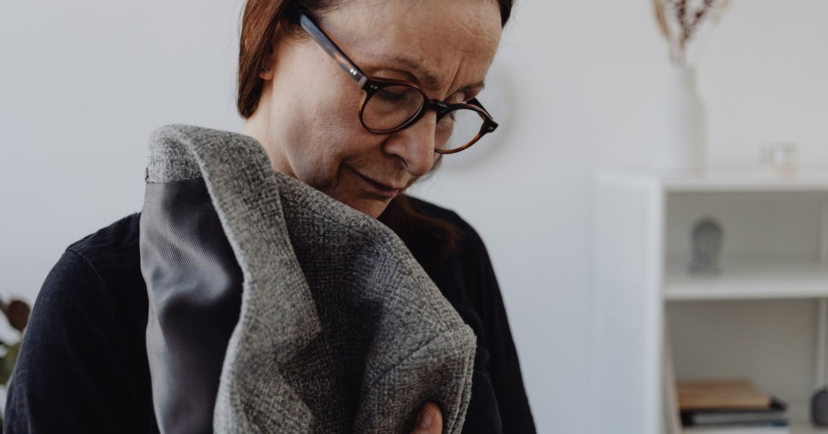 Senior woman embracing a coat, reflecting loneliness and introspection indoors.