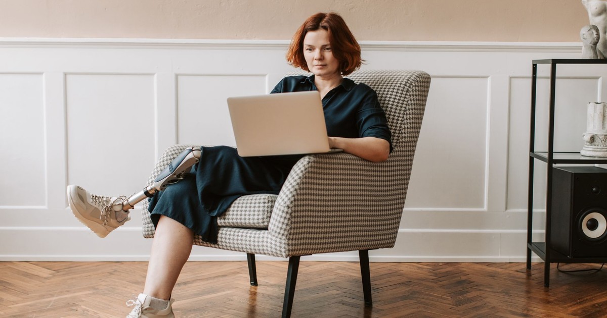Adult woman with prosthetic leg working on laptop in a stylish room, showcasing empowerment and modern lifestyle.