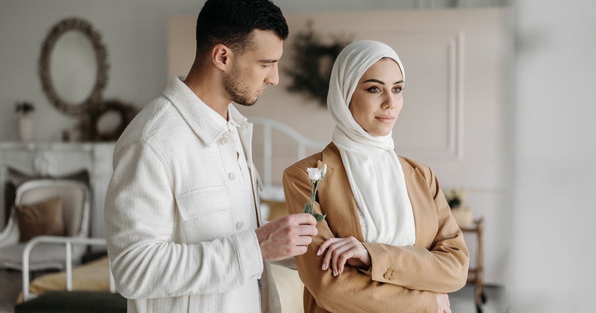 A man offering a flower to a woman in a hijab indoors, capturing a romantic moment.