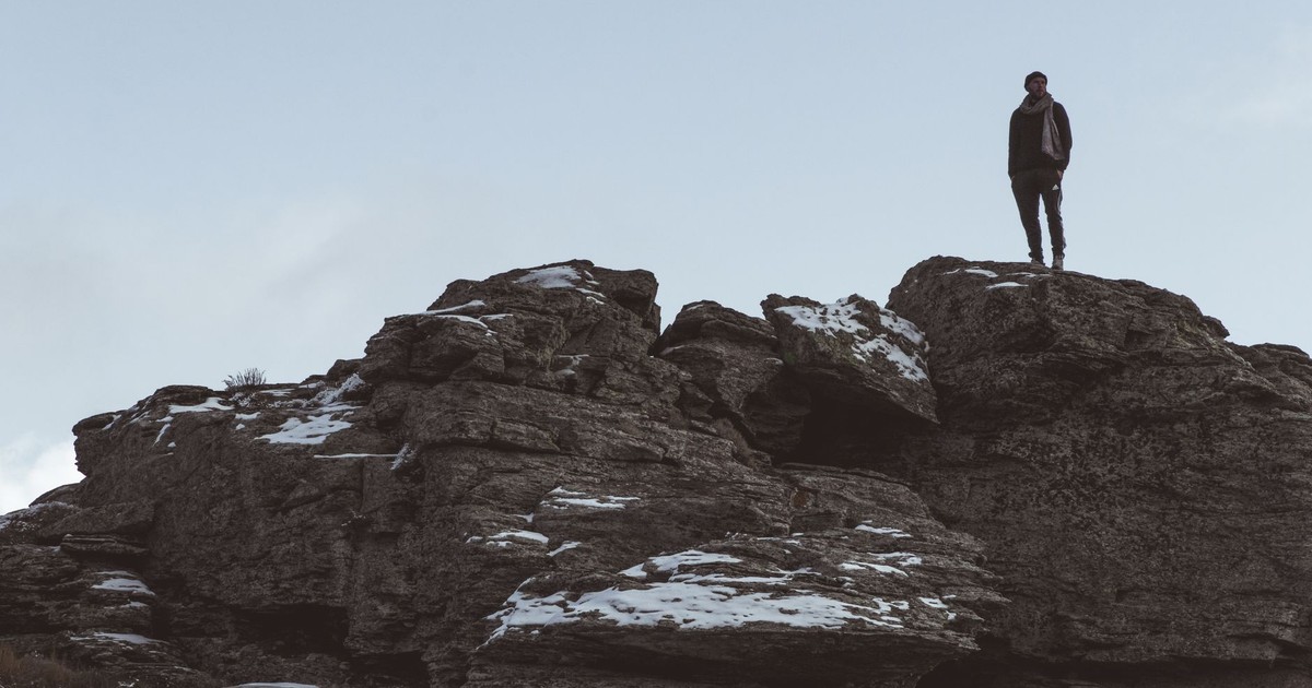 A man standing alone on a snowy rock outcrop under a clear sky, depicting solitude in nature.