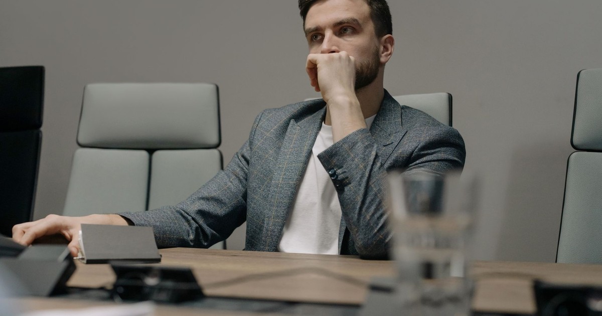 A contemplative businessman sitting at a meeting table in a modern office setting.