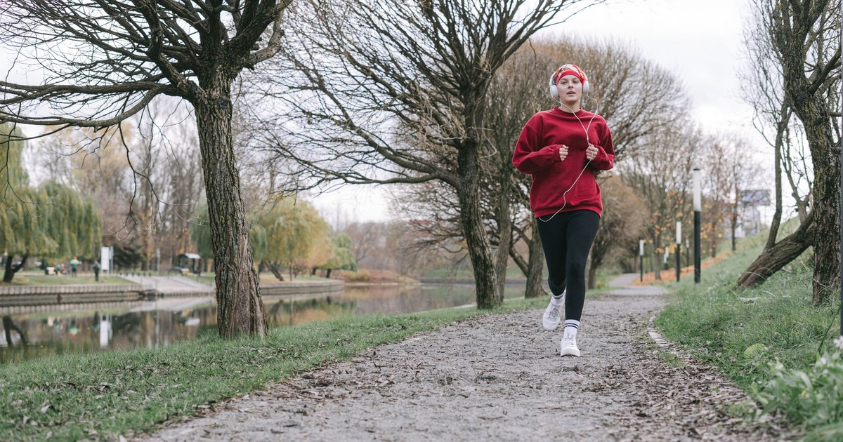 A woman in a red outfit jogs along a tree-lined path by a calm river, capturing an autumn fitness vibe.