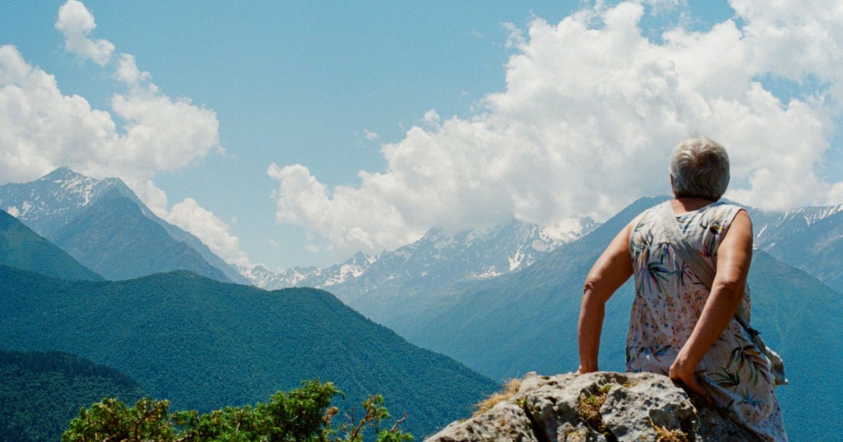 Elderly woman enjoying the view from the top of a mountain under a bright blue sky.