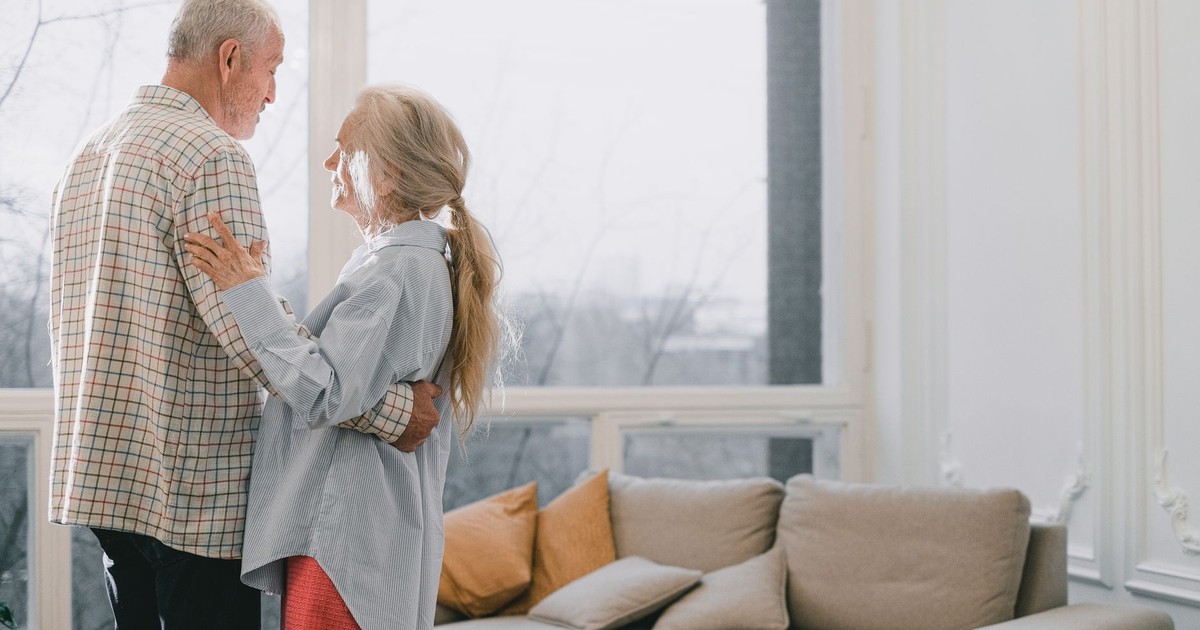 A senior couple shares a tender dance in a bright, cozy living room.