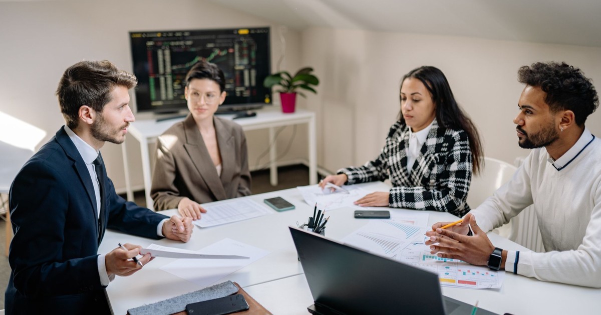 A diverse team of professionals engaged in a business meeting around a conference table with a laptop.