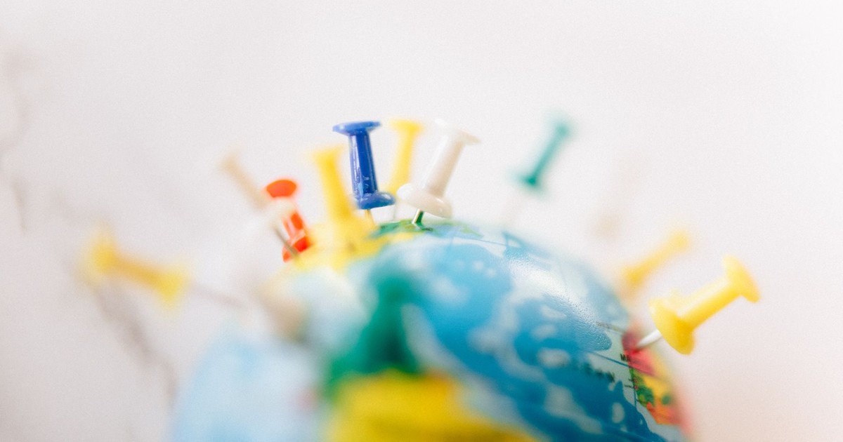 Vibrant close-up of a globe marked with multicolored push pins on a white background.