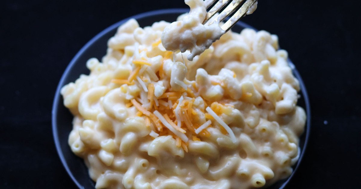 Delicious creamy mac and cheese topped with shredded cheese on a black plate.