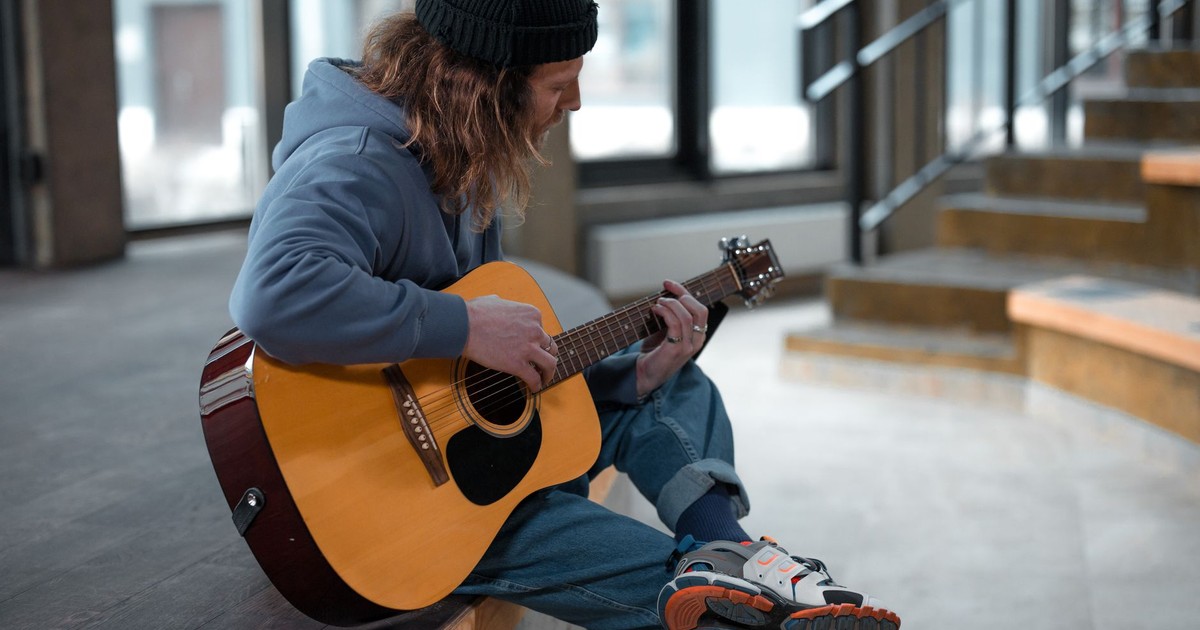 A man casually playing an acoustic guitar indoors on a staircase.