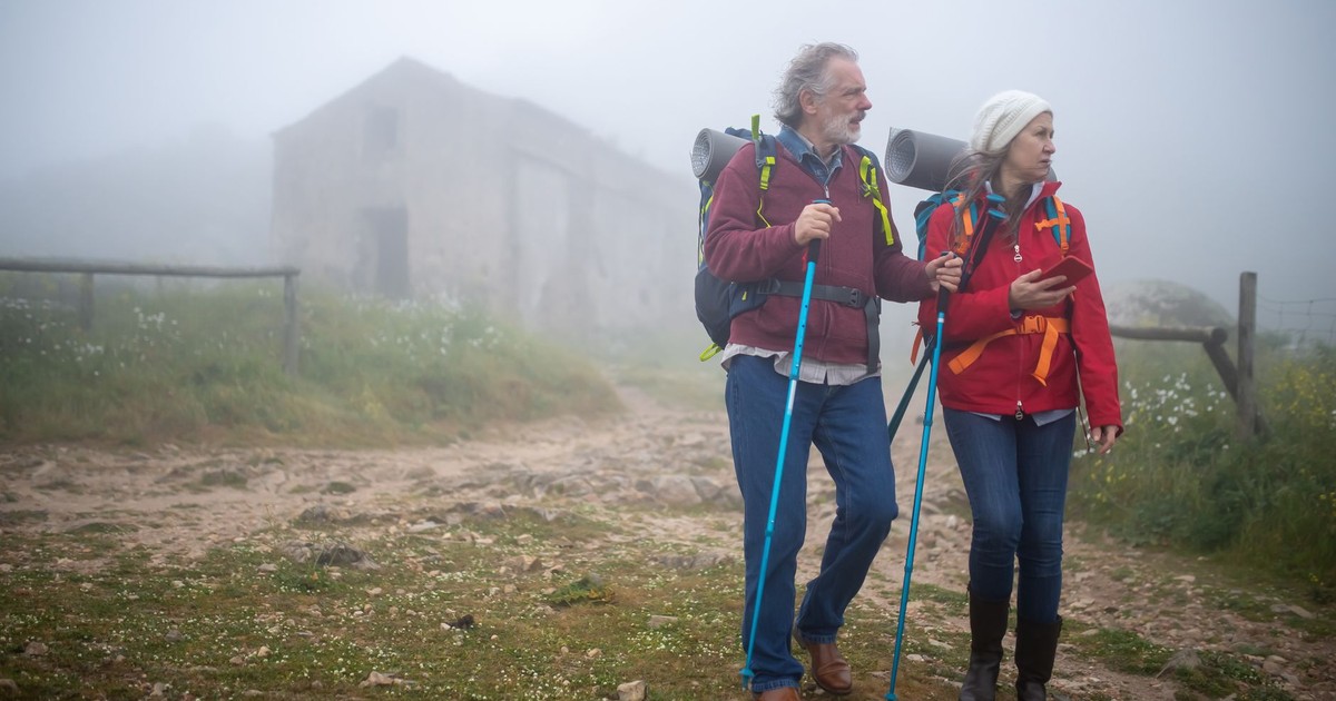 Elderly couple enjoying a foggy hike in rural Portugal, using trekking poles for support.