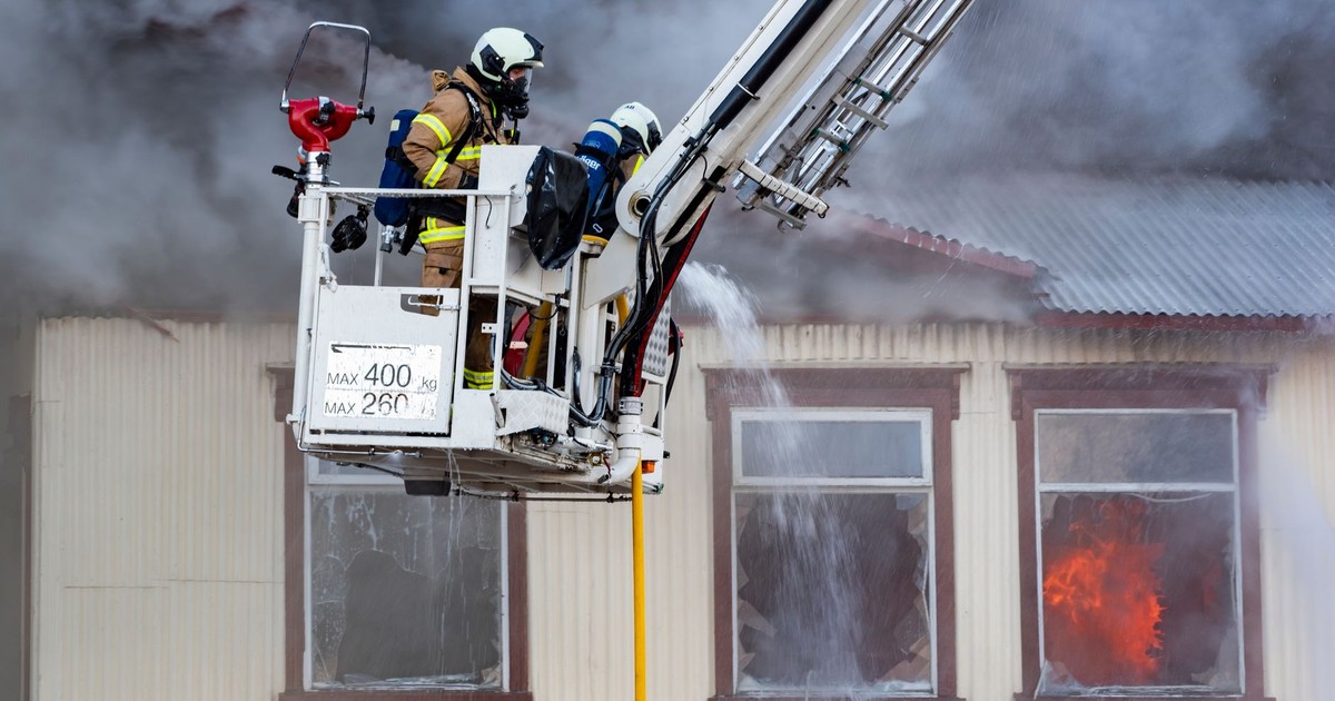 Firefighters on a ladder extinguishing a house fire with smoke and flames visible.