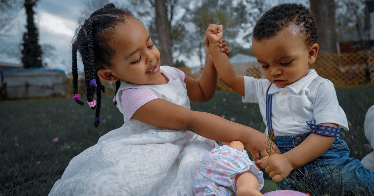 Two young children playing happily with toys outdoors in a sunlit garden.