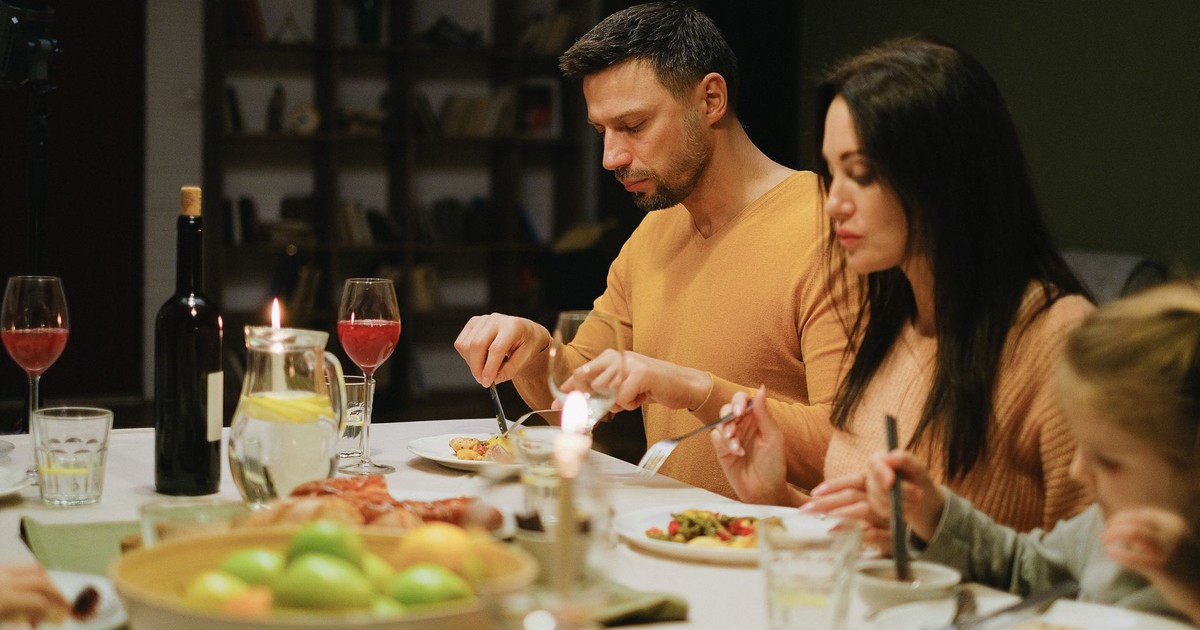 A family gathered around a dinner table indoors, enjoying a meal together with wine and candles.