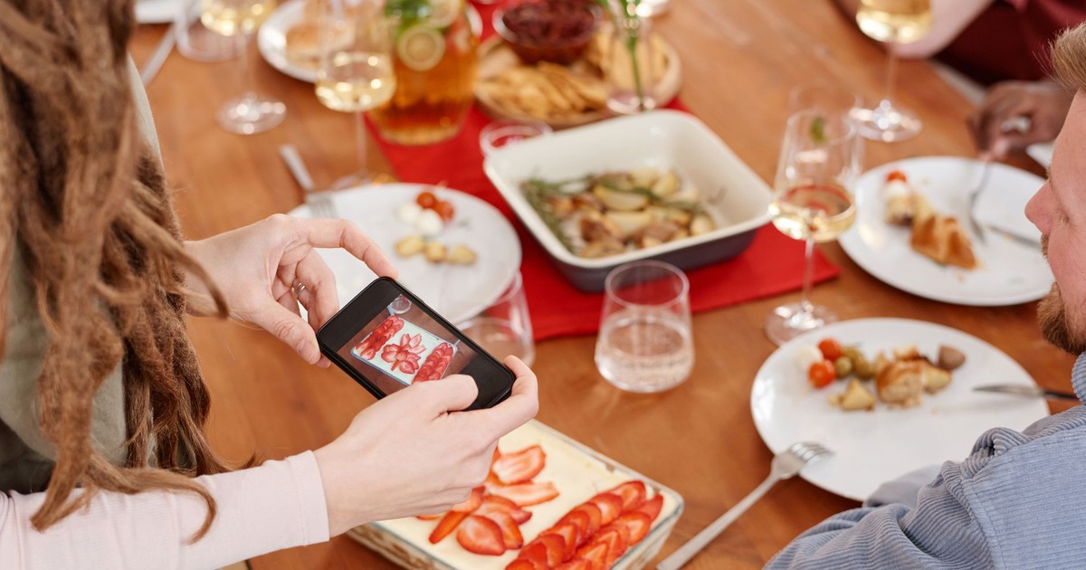 A person captures a photo of strawberry tiramisu at a lively dinner gathering.