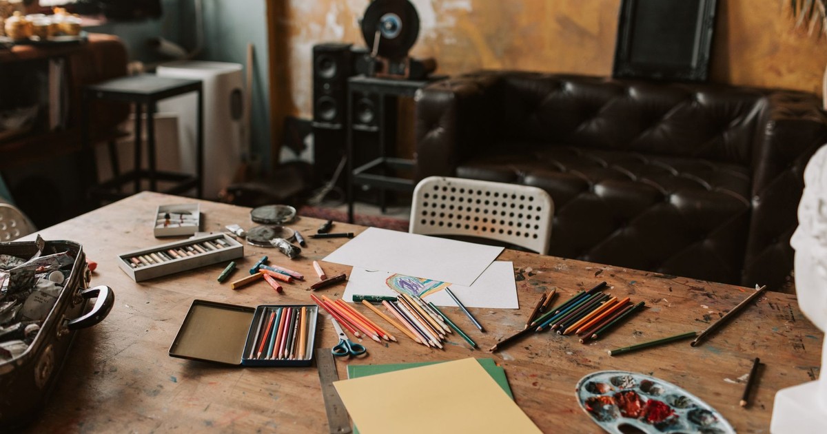 Art studio with colored pencils, paper, and various art materials on a rustic table.