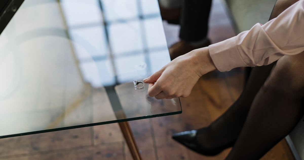 Close-up of a woman placing a wedding ring on a glass table, symbolizing relationship changes.