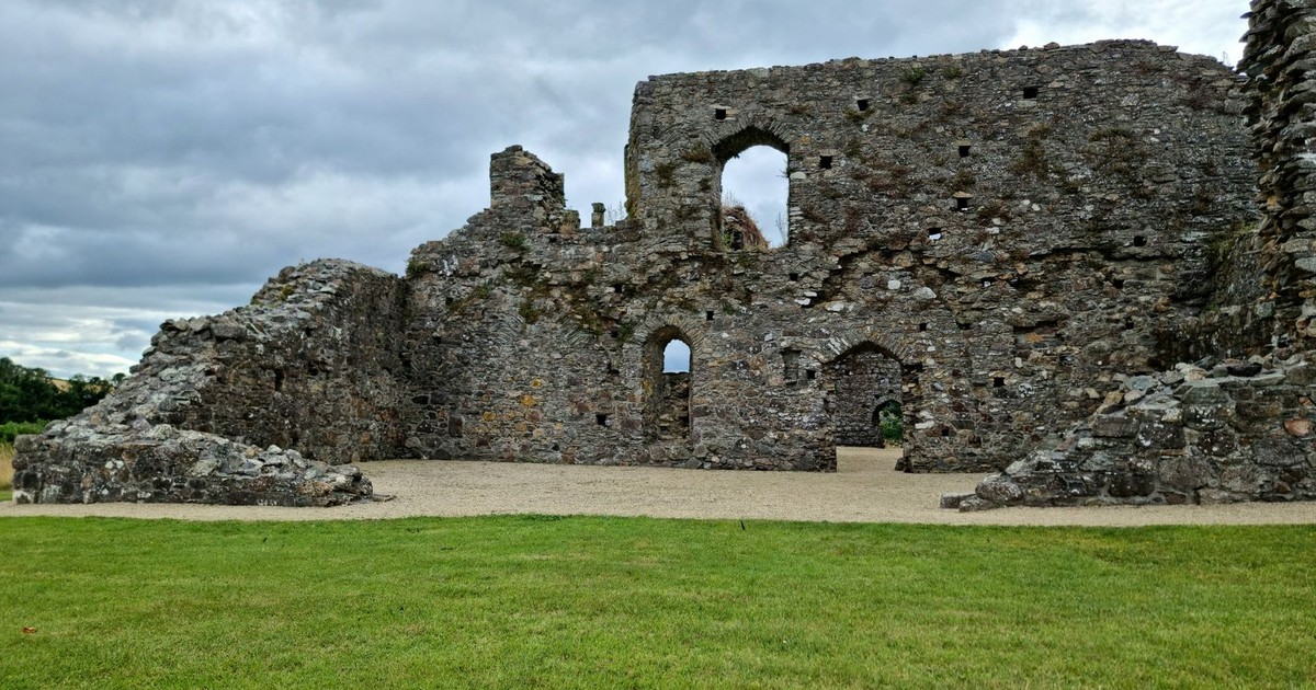 Explore the architectural charm of ancient stone ruins with large archways beneath a cloudy sky.