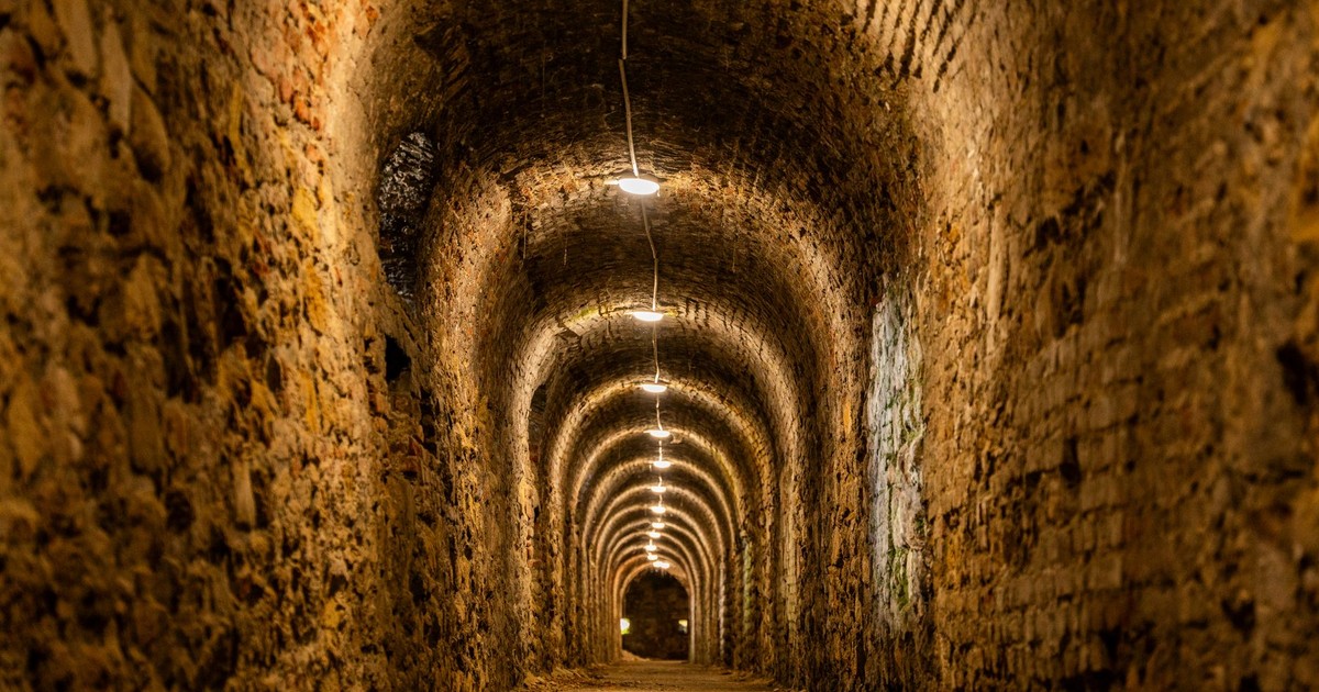 A dimly lit historic underground tunnel featuring brick archways, creating a mysterious ambiance.