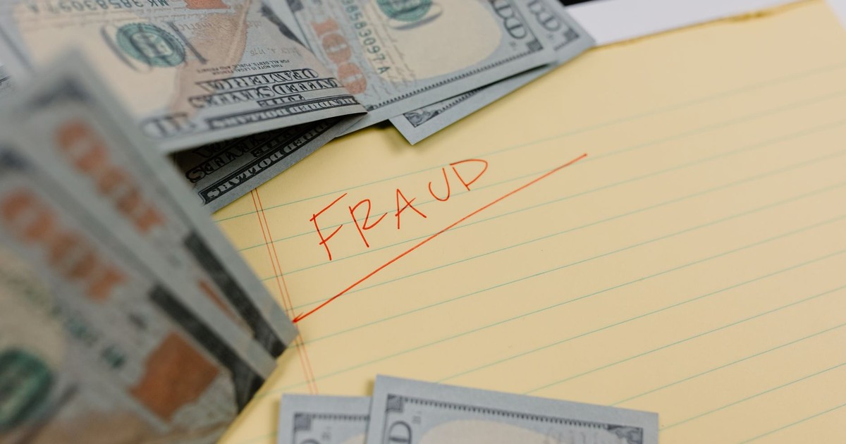 Close-up of US dollars and 'Fraud' written on yellow paper, representing financial scams.